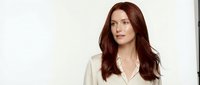 Professional businesswoman with long auburn hair wearing white blazer against neutral background for corporate marketing materials.