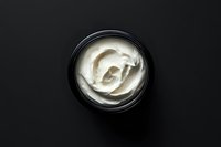 Luxury face cream in black jar with swirled white moisturizer texture on dark background for skincare and beauty product marketing campaigns.