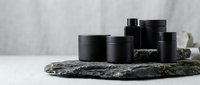 Black cosmetic jars arranged on natural stone surface with soft lighting for luxury skincare product presentation and spa branding concepts.
