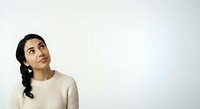 Young woman with dark braided hair and olive complexion wearing cream knit sweater, looking upward thoughtfully against white background, suitable for lifestyle and portrait design projects.