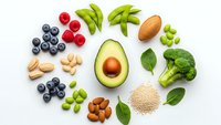 Fresh healthy foods arranged in circle on white background including avocado broccoli berries nuts and green vegetables for clean eating lifestyle.