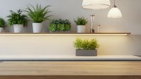 Modern kitchen counter with fresh green plants in white pots, wooden shelving and warm pendant lighting creating cozy cooking space atmosphere.