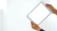Person of South Asian descent holding tablet with blank white screen against neutral background, suitable for app mockups and digital marketing.