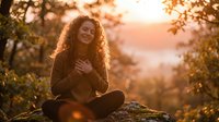 Young woman with curly hair sitting peacefully outdoors during golden hour sunset, enjoying nature and mindfulness moment in warm autumn light.