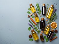 Essential oils in glass bottles with cork stoppers surrounded by fresh herbs, spices and citrus on textured background for aromatherapy and wellness.
