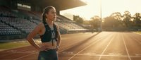 Young athletic woman jogging on running track during golden hour sunset at stadium. Fitness training concept for healthy lifestyle and sports activities.