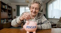 Senior Caucasian woman with glasses putting coin into pink piggy bank labeled pension at home desk, retirement savings and financial planning concept.