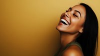 Young African American woman with bright genuine smile and closed eyes expressing joy and happiness against golden background. Professional portrait for wellness and lifestyle content.
