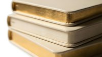 Stack of elegant notebooks with gold and cream covers arranged on white background, perfect for stationery, education, and lifestyle concepts.