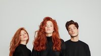 Young diverse models wearing black turtleneck sweaters pose against light background, two redhead women and brunette man with modern hairstyles in minimalist studio setting.