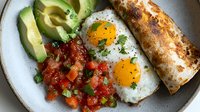 Sunny side up eggs served with fresh pico de gallo, sliced avocado and grilled tortilla on rustic ceramic plate. Mexican breakfast or brunch setting.