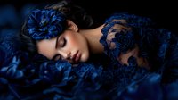 Young woman with closed eyes resting among deep blue lace and floral decorations against dark background, creating dreamy romantic atmosphere for fashion photography.
