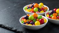 Colorful round candies in white bowls on dark slate surface. Sweet treats for parties, celebrations, and confectionery displays.