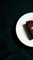 Slice of rich chocolate cake on white plate against dark teal textured background, overhead view for bakery, dessert, and food styling projects.
