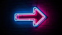Bright neon arrow sign glowing pink and blue against dark brick wall for nightclub, bar, restaurant, retail store directional signage and advertising.