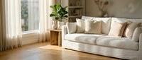 Modern bright living room interior with white sofa, wooden floors, and natural light streaming through windows creating cozy home atmosphere.