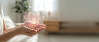 Hands holding glowing pink lotus flower hologram in bright room with blurred background, symbolizing wellness, spirituality, healing energy and meditation practice.