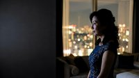 Elegant young woman in blue dress standing by window with city lights at night, contemplative mood for lifestyle and fashion concepts.