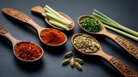 Aromatic spices and herbs in wooden spoons with fresh lemongrass on dark slate background for culinary cooking and seasoning recipes.