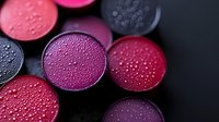 Colorful makeup eyeshadow palette with water droplets on surface, featuring vibrant red, purple, and black circular pans in close-up view.