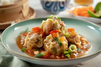 Steamed dumplings with vegetables in savory Asian sauce garnished with green onions and carrots served on turquoise ceramic plate, close up food photography.