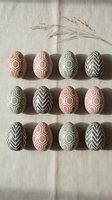 Decorative Easter eggs with geometric patterns in pink and sage green colors arranged on neutral linen fabric with wheat stems for spring holiday celebration.