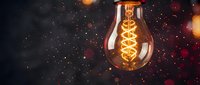 Vintage Edison bulb with glowing filament against dark starry background with warm bokeh lights creating atmospheric mood for creative projects.
