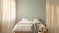 Modern minimalist bedroom interior with wooden bed frame, white bedding, sage green throw blanket, wicker basket, and natural light filtering through curtains.