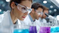 Laboratory researcher in protective eyewear examining colorful liquid samples in test tubes while working with colleagues in modern scientific facility.