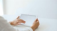 Woman holding tablet with blank screen, wearing white clothing, hands visible in close-up view. Suitable for technology, business, and digital communication concepts.