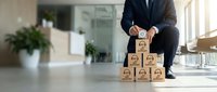 Professional businessman in suit stacking wooden blocks with star rating symbols in modern office environment for customer service excellence concept.