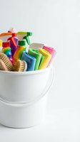 White bucket filled with colorful cleaning supplies including spray bottles, sponges and brushes for household chores and spring cleaning tasks.