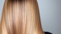 Straight blonde hair close up with smooth silky texture and natural highlights against dark background, demonstrating professional hair care and styling results.
