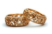 Ornate rose gold wedding bands featuring intricate floral and scroll filigree pattern design on white background, luxury jewelry photography for bridal collections.