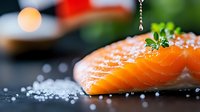 Fresh salmon fillet with sea salt and herbs on dark slate board. Premium seafood ingredient for gourmet cooking and healthy meal preparation.