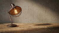 Vintage desk lamp with wire cage shade casting warm glow on wooden table against textured concrete wall, suitable for interior design and workspace styling projects.