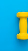 Yellow dumbbell weight on bright blue background, isolated fitness equipment for gym, sports, and wellness design projects.