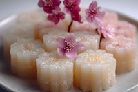Traditional Asian mochi rice cakes with pink cherry blossoms on white plate. Sweet dessert confectionery for tea ceremony celebrations and cultural events.