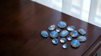 Blue labradorite gemstones collection scattered on wooden table surface near window with natural daylight illumination for jewelry making projects.