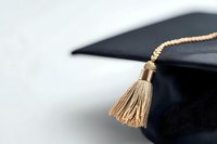 Black graduation mortarboard cap with gold tassel against white background, closeup view showing academic achievement and educational success.