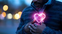 Glowing pink neon heart shape floating between hands of African American man in sweater against blurred city lights bokeh background at night.