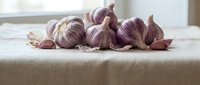 Fresh garlic cloves with papery skin scattered on neutral linen fabric, suitable for culinary, food styling, and cooking-related projects.