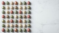 Colorful speckled eggs arranged in neat grid pattern on white marble surface for Easter celebration and spring holiday decorating projects.