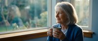 Senior Caucasian woman with gray hair enjoying morning coffee by window, peaceful retirement lifestyle, cozy home interior with natural light.
