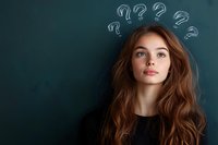 Young woman with long brown wavy hair looking thoughtful against dark green chalkboard background with question marks drawn above her head, expressing confusion or curiosity.