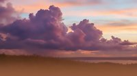 Dramatic sunset clouds over tranquil beach with golden sand dunes and grass creating peaceful coastal landscape for relaxation and travel concepts.