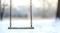 Empty wooden swing on chains against blurred winter background with snow, creating nostalgic and peaceful atmosphere in abandoned playground.