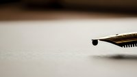 Fountain pen nib with ink drop on white paper surface, close-up macro shot for writing, calligraphy, literature and business communication concepts.