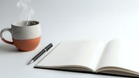 Steaming coffee mug with open notebook and pen on clean white desk creating peaceful morning workspace for writing and planning daily tasks.