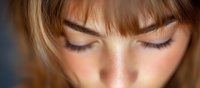 Close up view of young caucasian woman with closed eyes, natural makeup, freckles and brown bangs showing peaceful expression and relaxed state.